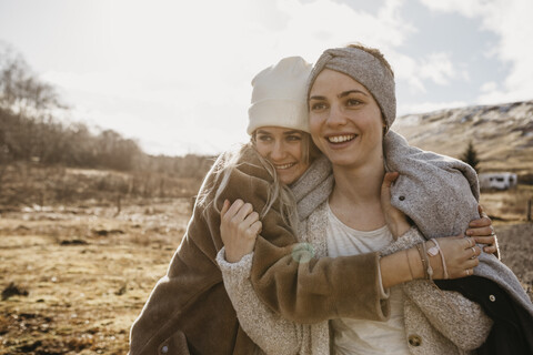 UK, Schottland, glückliche Freundinnen, die sich in einer ländlichen Landschaft umarmen, lizenzfreies Stockfoto