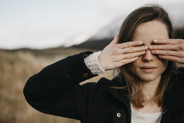 UK, Schottland, junge Frau, die ihre Augen in einer ländlichen Landschaft bedeckt - LHPF00554