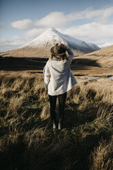 Großbritannien, Schottland, Loch Lomond and the Trossachs National Park, Rückansicht einer jungen Frau, die in einer ländlichen Landschaft steht und auf einen Berg schaut - LHPF00565