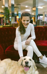 Lächelnde Frau mit Hund, die auf einer Couch in einem Vintage-Laden sitzt - MGOF03993
