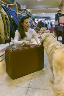 Frau mit Hund und altmodischem Koffer in einer Vintage-Boutique - MGOF04003