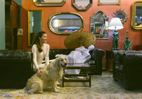 Lächelnde Frau mit Hund, die auf einer Couch in einem Vintage-Laden sitzt - MGOF04008