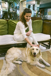 Lächelnde Frau mit Hund, die auf einer Couch in einem Vintage-Laden sitzt - MGOF04024