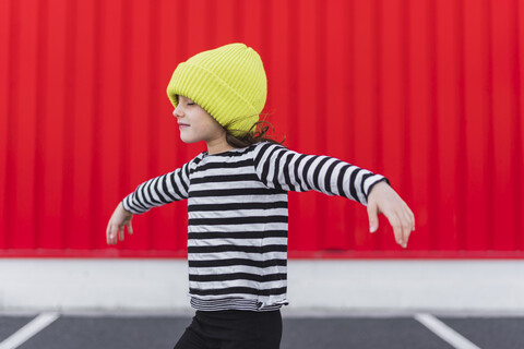 Kleines Mädchen mit gestreiftem Hemd und gelber Mütze beim Balancieren, lizenzfreies Stockfoto