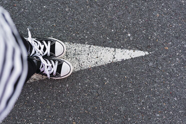 Girl wearing sneakers standing on arrow sign on lane, top view - ERRF01181