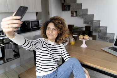 Frau sitzt zu Hause und macht ein Selfie mit ihrem Smartphone - FMOF00597