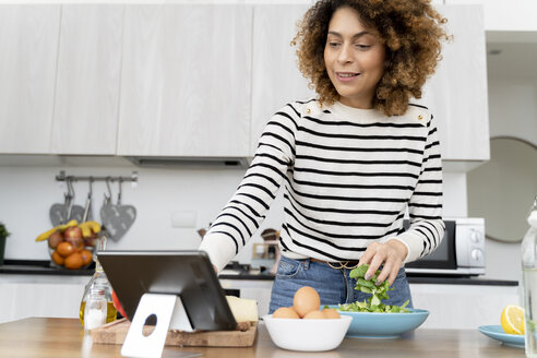 Woman standing in kitchen, preparing salad for lunch - FMOF00604