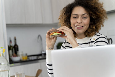Frau benutzt Laptop, während sie ein Sandwich isst - FMOF00611