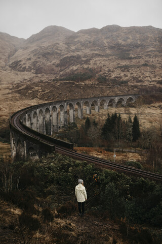UK, Schottland, Highland, Glenfinnan Viaduct, Rückansicht einer jungen Frau mit Blick auf die Aussicht, lizenzfreies Stockfoto