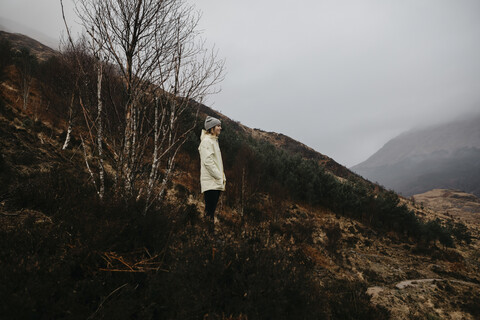 Großbritannien, Schottland, Highland, junge Frau in ländlicher Landschaft stehend mit Blick auf die Landschaft, lizenzfreies Stockfoto