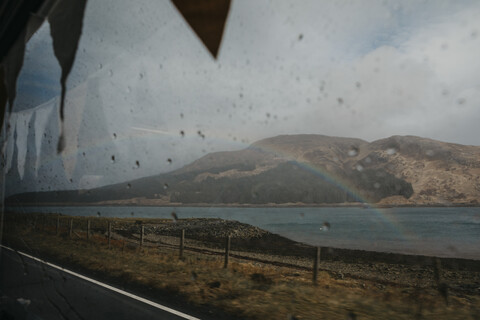 UK, Schottland, Highland, Regenbogen über dem Meer durch Autofenster gesehen, lizenzfreies Stockfoto