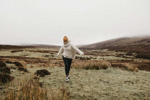 UK, Schottland, Isle of Skye, glückliche junge Frau, die in ländlicher Landschaft läuft, lizenzfreies Stockfoto