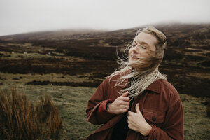 UK, Schottland, Highland, Porträt einer jungen Frau mit vom Wind zerzaustem Haar in einer ländlichen Landschaft - LHPF00620