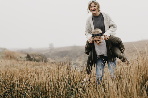 UK, Schottland, Isle of Skye, glückliche Frau trägt Freund Huckepack in ländlicher Landschaft, lizenzfreies Stockfoto