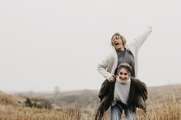 UK, Scotland, Isle of Skye, happy woman carrying friend piggyback in rural landscape - LHPF00628