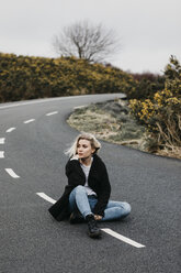 Großbritannien, Schottland, Isle of Skye, junge Frau auf Landstraße sitzend - LHPF00636