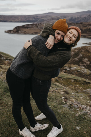 UK, Schottland, Highland, glückliche Freundinnen umarmen sich in ländlicher Landschaft, lizenzfreies Stockfoto