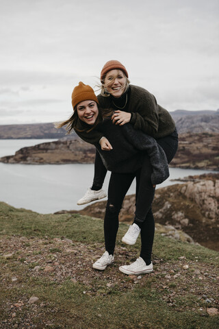 UK, Schottland, Highland, glückliche Frau trägt Freund Huckepack in ländlicher Landschaft, lizenzfreies Stockfoto