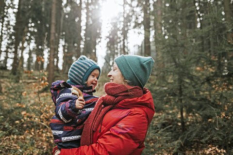 Mutter trägt glückliche kleine Tochter im herbstlichen Wald, lizenzfreies Stockfoto
