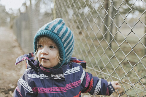 Toddler girl in warm clothes at a fence in forest - DWF00423