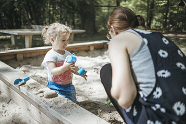 Mother playing with little daughter in sandbox on a playground - DWF00435