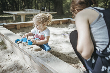 Mother playing with little daughter in sandbox on a playground - DWF00436