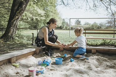 Mother playing with little daughter in sandbox on a playground - DWF00437