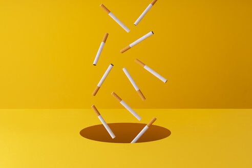 Cigarettes falling into a hole in yellow background - DRBF00154