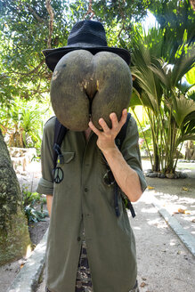 Seychellen, Mann versteckt sein Gesicht hinter einem riesigen Samen von Coco de Mer - NDF00887