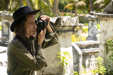 Seychellen, La Digue, Mann fotografiert Grabsteine auf altem Friedhof - NDF00893