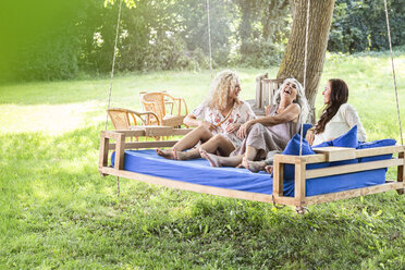 Frauen einer Familie entspannen sich im Garten, sitzen auf einem Schaukelbett - PESF01605