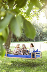Women of a family relaxing in garden, sitting on a swing bed - PESF01607