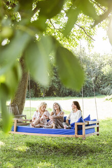 Frauen einer Familie entspannen sich im Garten, sitzen auf einem Schaukelbett - PESF01607