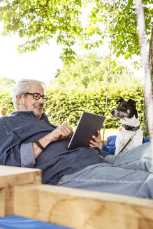 Ein älterer Mann entspannt sich auf einem Schaukelbett in seinem Garten und benutzt ein digitales Tablet - PESF01617