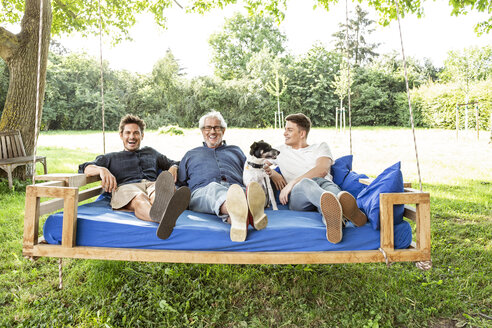 Männer einer Familie, die auf einem Schaukelbett im Garten sitzen und sich unterhalten - PESF01621