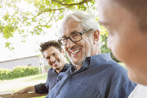 Men of a family sitting on a swing bed ing the garden, talking - PESF01623