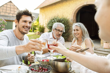 Eine glückliche Familie, die gemeinsam im Garten isst und mit Gläsern anstößt - PESF01640