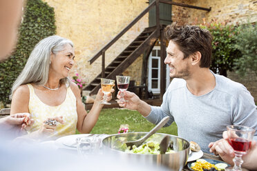 Eine glückliche Familie, die gemeinsam im Garten isst und mit Gläsern anstößt - PESF01644