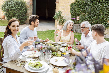 Eine glückliche Familie, die gemeinsam im Garten isst und mit Gläsern anstößt - PESF01645