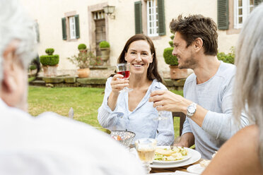 Eine glückliche Familie, die gemeinsam im Garten isst und mit Gläsern anstößt - PESF01647