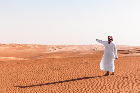 Beduine in Nationaltracht in der Wüste stehend, in die Ferne zeigend, Wahiba Sands, Oman - WVF01359