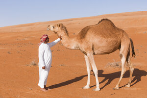 Beduine streichelt sein Kamel in der Wüste, Wahiba Sands, Oman - WVF01361