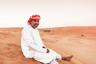 Beduine in Nationaltracht auf einer Sanddüne in der Wüste sitzend, Wahiba Sands, Oman - WVF01409