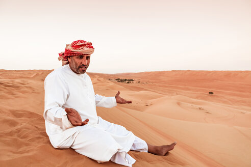 Beduine in Nationaltracht auf einer Sanddüne in der Wüste sitzend, Wahiba Sands, Oman - WVF01410