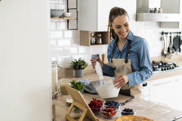 Young woman preparing a cream cake, using tablet - GIOF06185