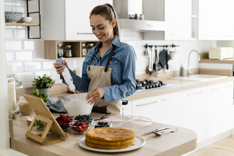 Junge Frau bei der Zubereitung einer Sahnetorte, mit Tablet, lizenzfreies Stockfoto