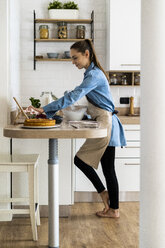 Young woman preparing a cream cake, using tablet - GIOF06194