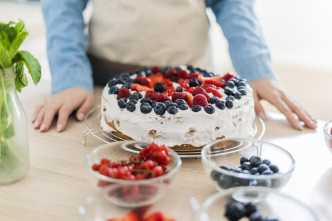 Junge Frau bereitet eine Sahnetorte mit frischen Früchten zu, lizenzfreies Stockfoto