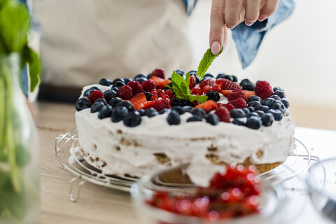 Junge Frau bereitet eine Sahnetorte mit frischen Früchten zu, lizenzfreies Stockfoto