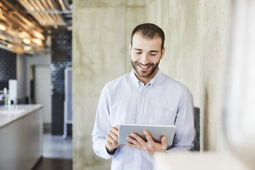 Smiling businessman using tablet in modern office - FMKF05550